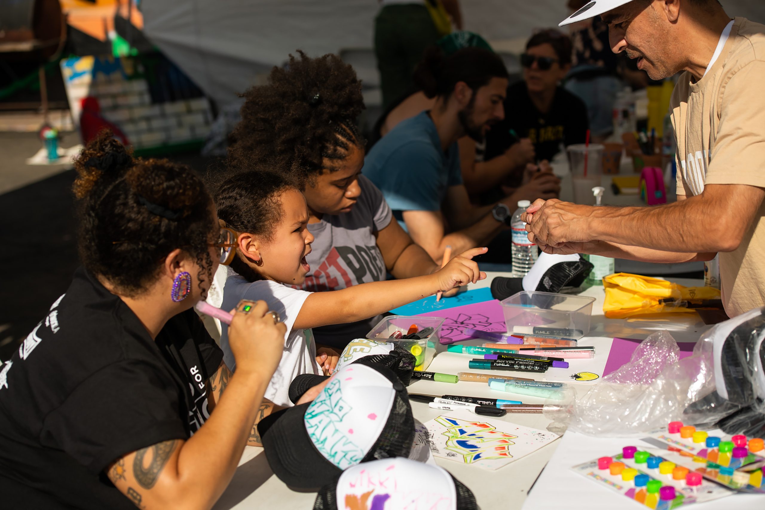 A photograph of members of the Arts for Healing and Justice Network and LA Youth Uprising Coalition community make art at a table covered with art supplies.